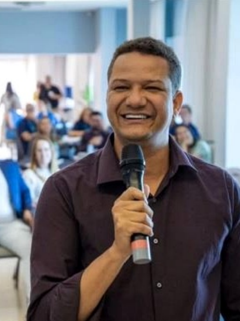 Eduardo Loureiro sorrindo durante uma palestra, com camisa social escura e microfone